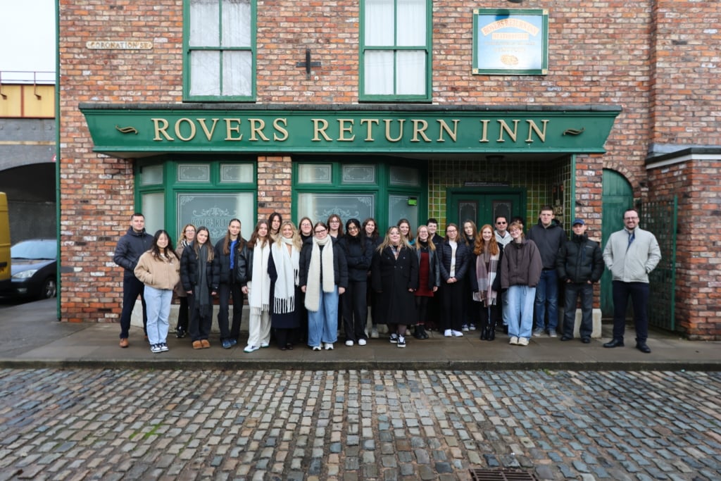 a group of university of sheffield students smile on the coronation street set outside the fictional pub 'the rovers return'